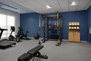Un gimnàs amb equip d'exercici, una banca, una pica de squat i una prestatgeria fixa a la paret amb tovalloles.