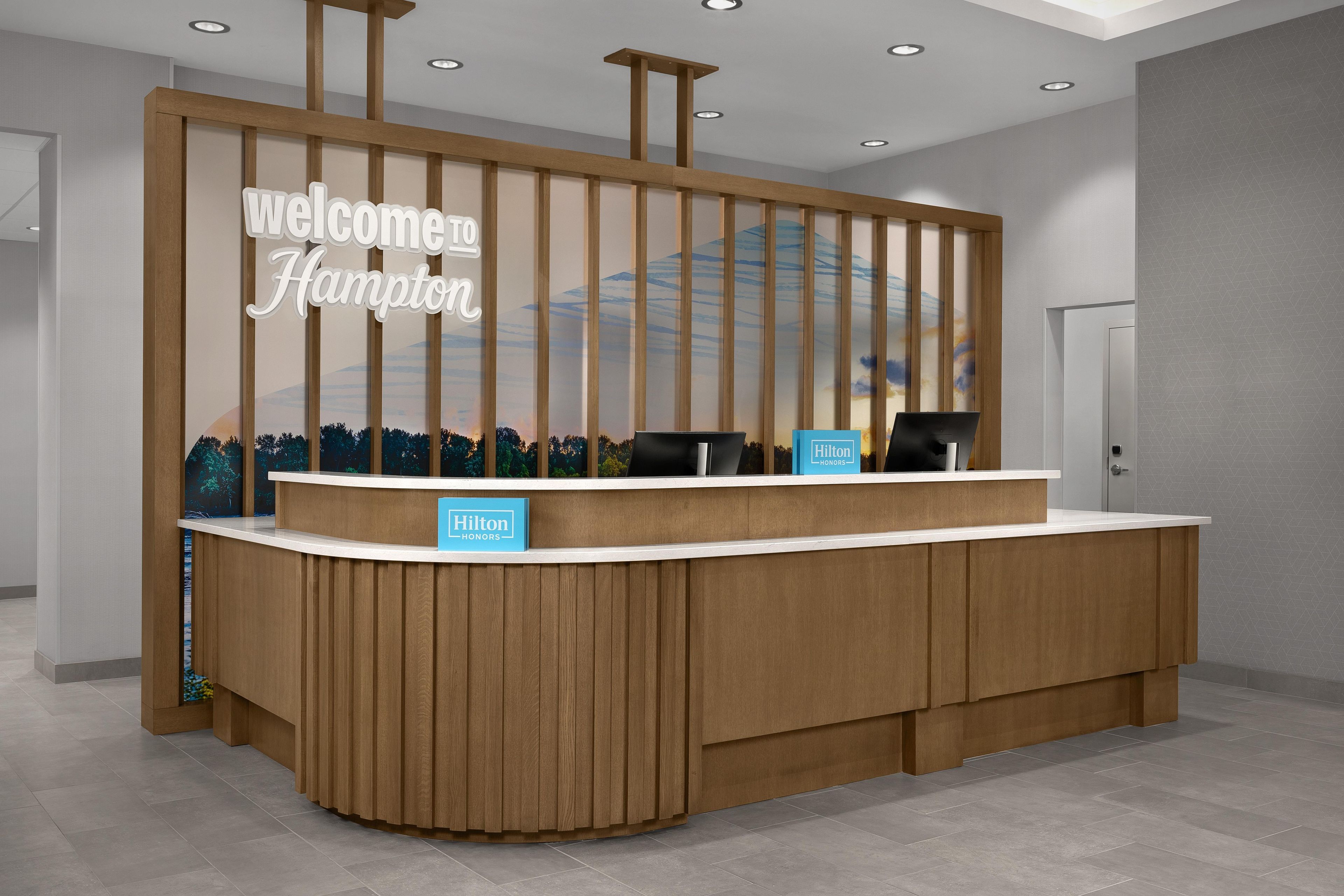 A reception desk with a 'Welcome Hampton' sign, two black chairs, and a 'Hilton Honors' sign.