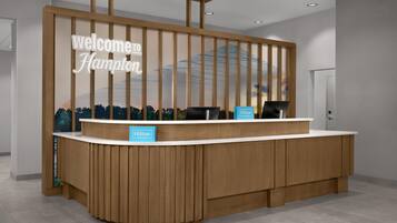 A reception desk with a 'Welcome Hampton' sign, two black chairs, and a 'Hilton Honors' sign.