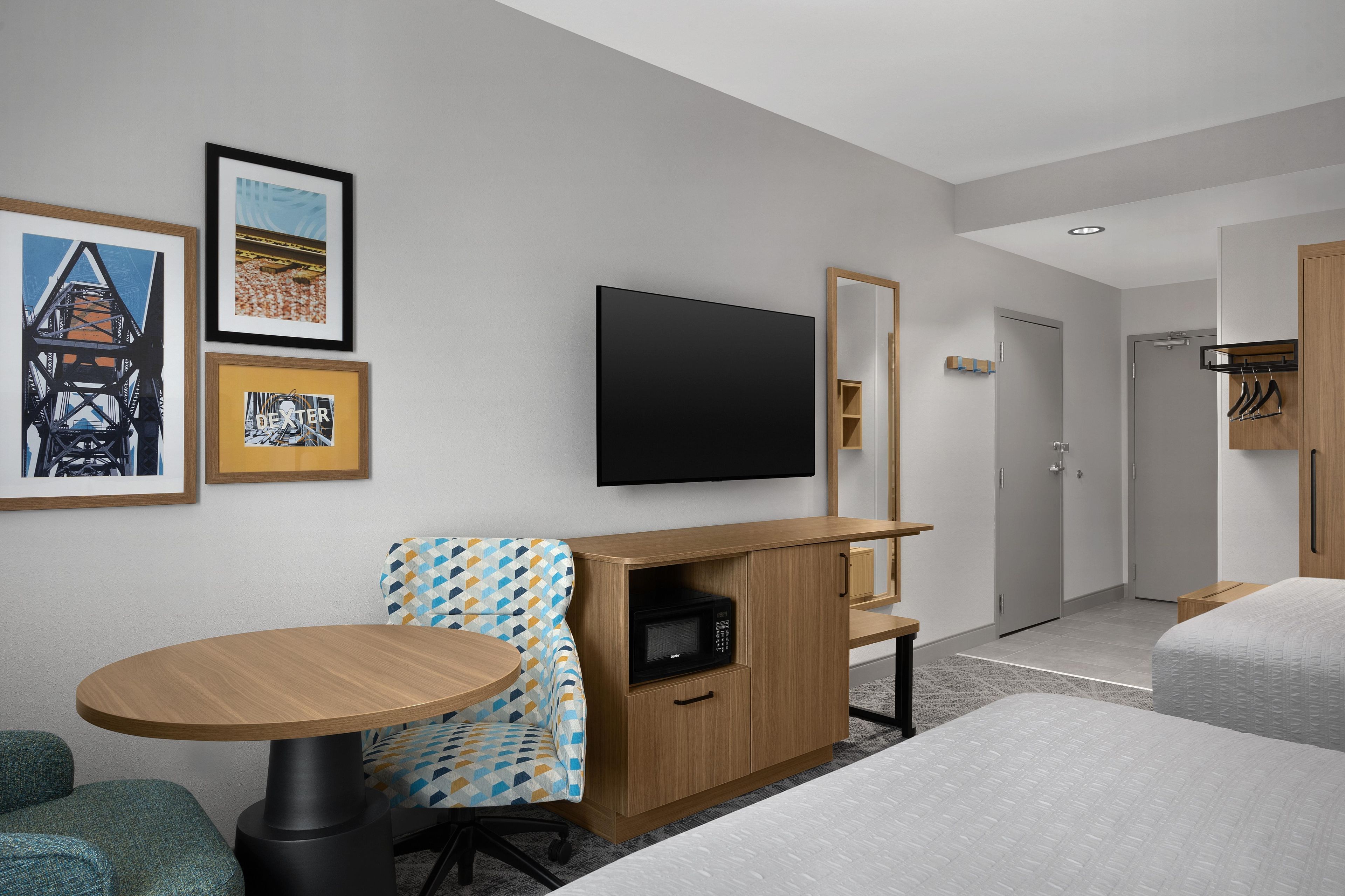 A hotel room with a flat-screen TV, a wooden desk, a sofa, a microwave, and a bed.