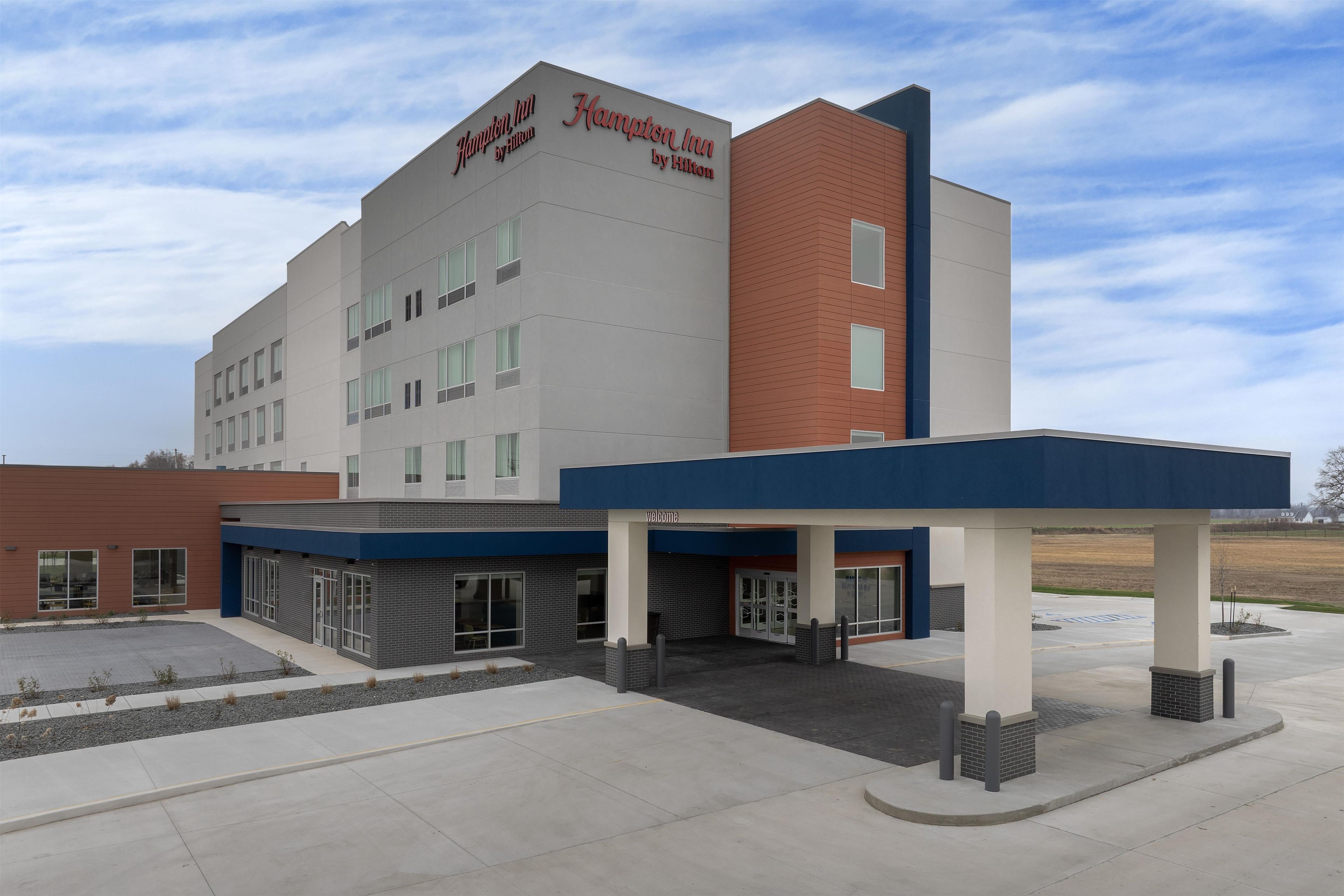 A Hampton Inn by Hilton hotel with a modern design, featuring a flat roof, large windows, and a welcoming entrance.