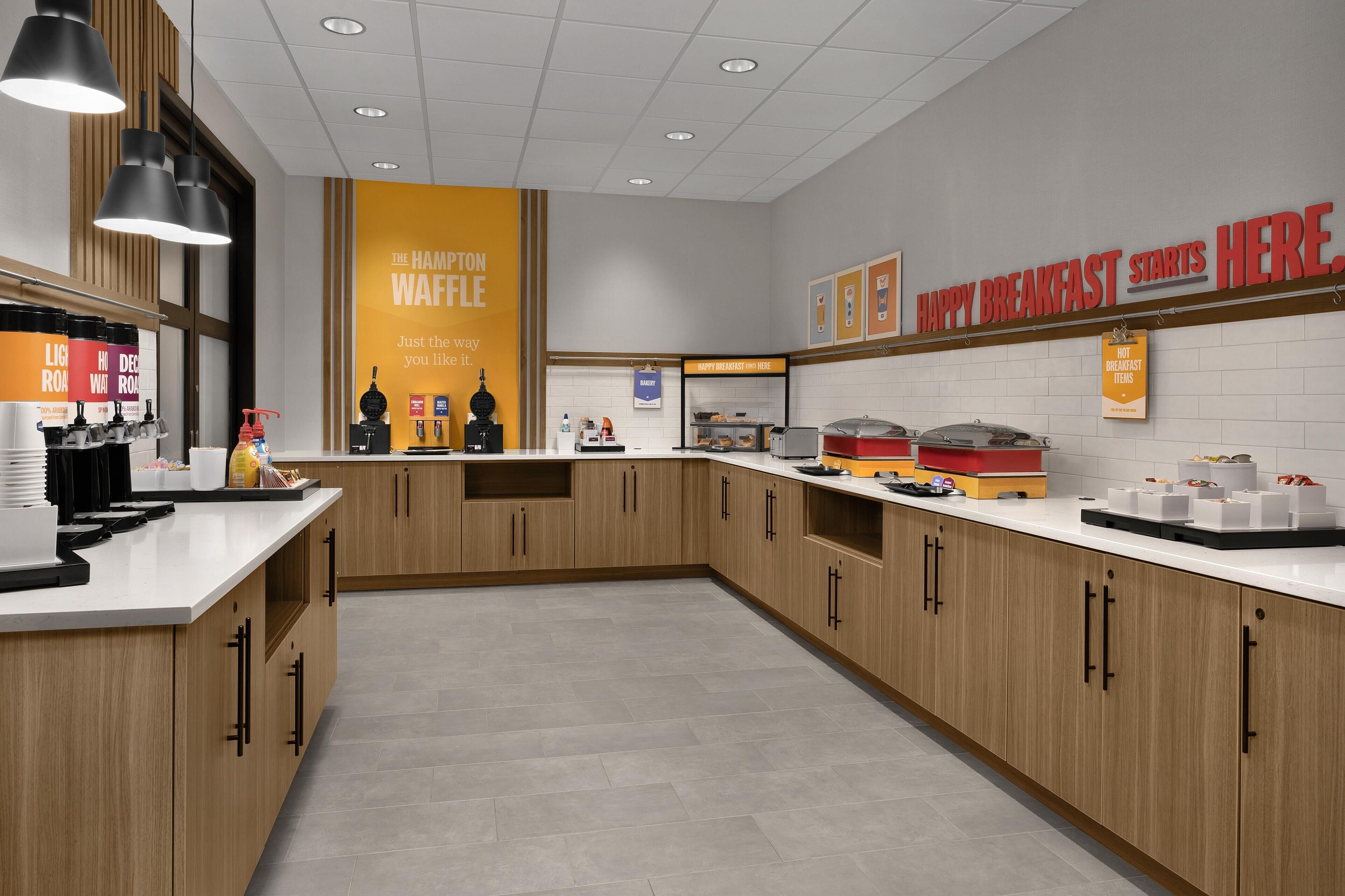Une cuisine moderne avec des meubles en bois, un plan de travail blanc et un coin dédié à la préparation de gaufres.