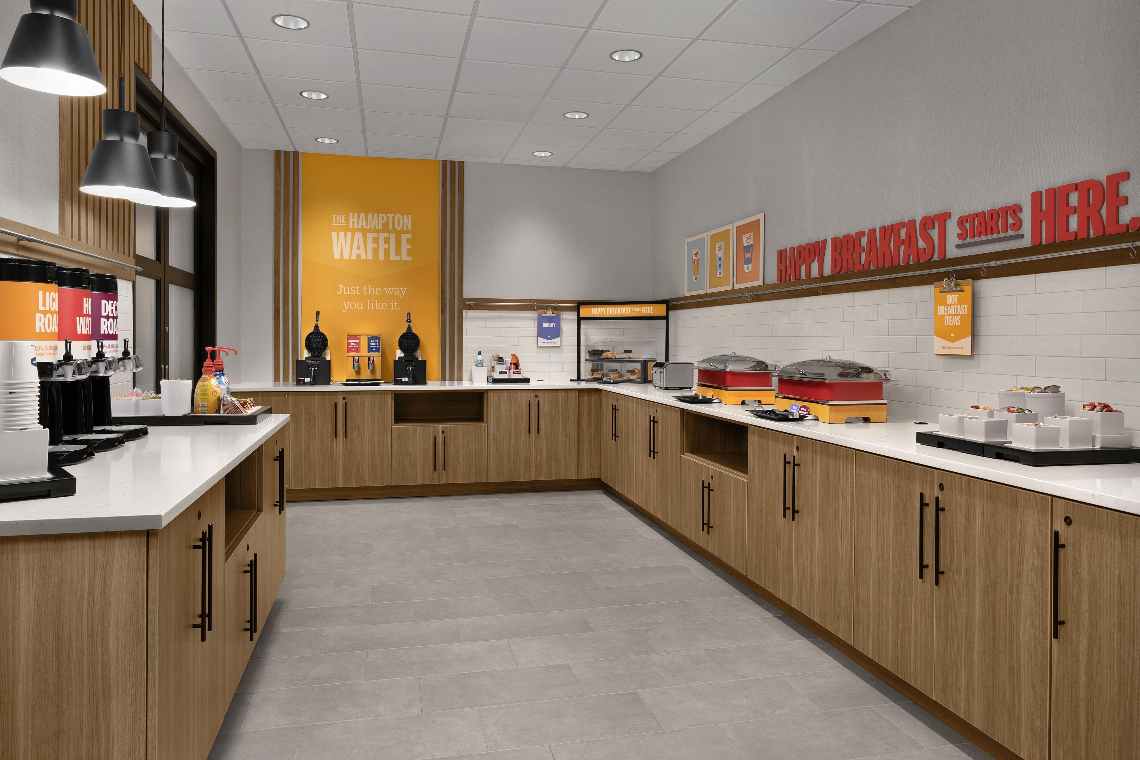 Una cocina moderna con armarios de madera, una estación de waffles y productos para el desayuno expuestos en la encimera.