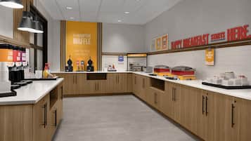 Cozinha moderna com armários de madeira, estação de waffles e alimentos de café da manhã dispostos no balcão.