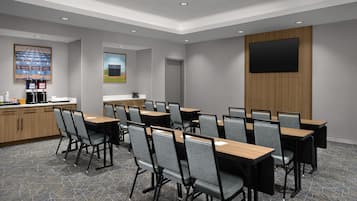 A conference room with tables and chairs, a coffee station, a painting, and a TV on the wall.