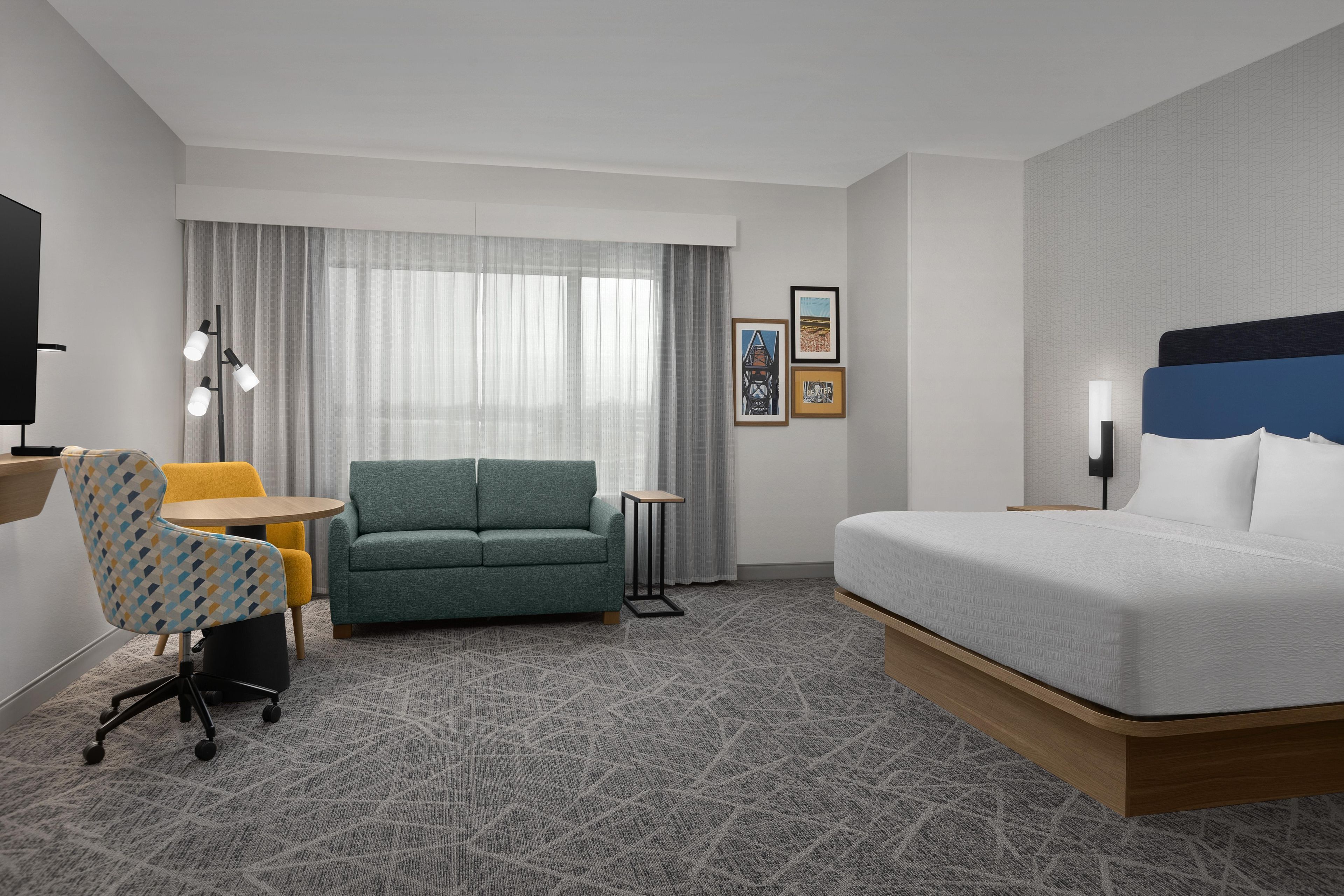 A hotel room with a bed, a sofa, a desk, a chair, and a TV.