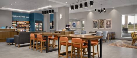 A modern hotel lobby with a central dining area, a minibar, and a view of the outdoors.