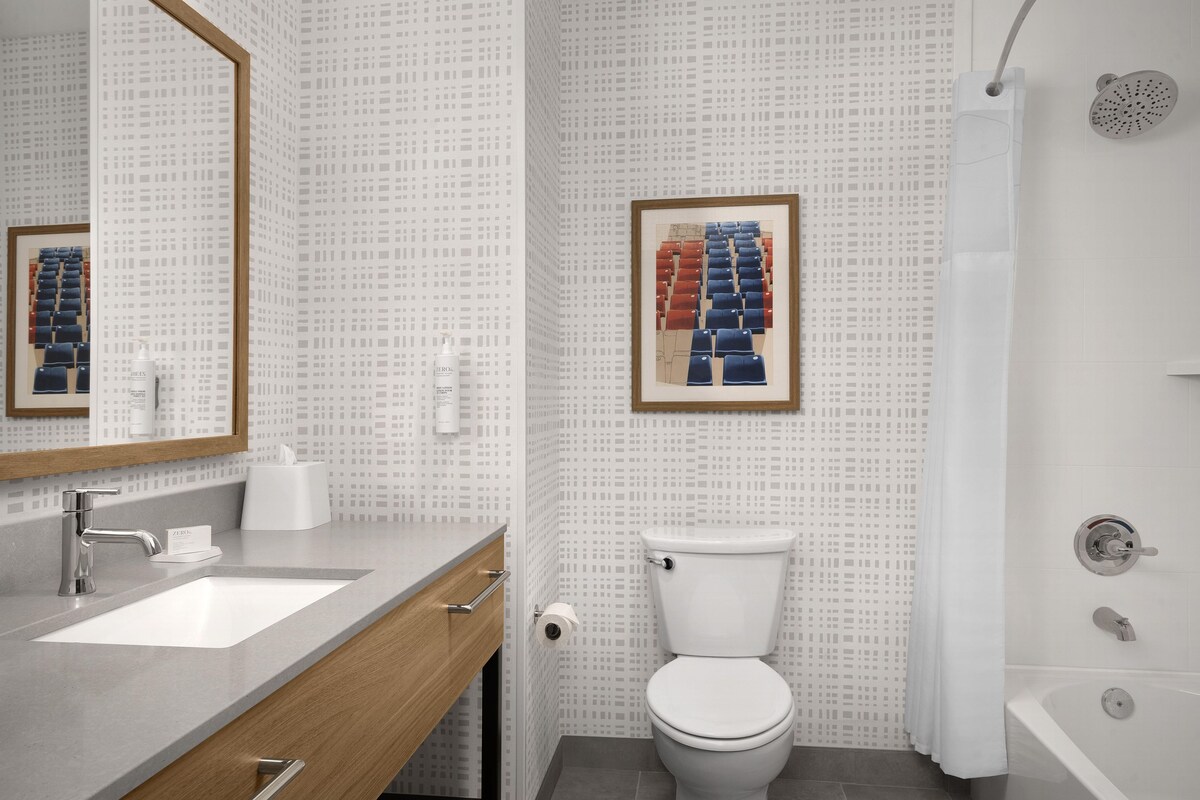 A bathroom with a modern design, featuring a large mirror, a sink, a toilet, and a bathtub.