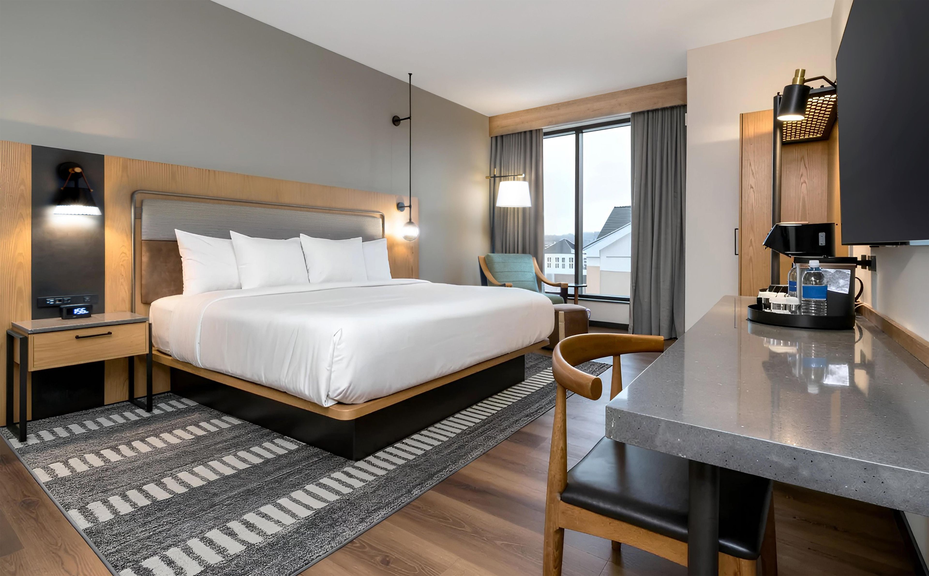 A hotel room with a bed, bedside table, lamp, chair, desk, and a television.