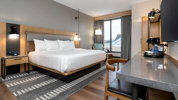 A hotel room with a bed, bedside table, lamp, chair, desk, and a television.