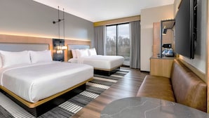 Ein Hotelzimmer mit zwei Betten, einem Schlafsofa, einem Fernseher und einer Kaffeemaschine.