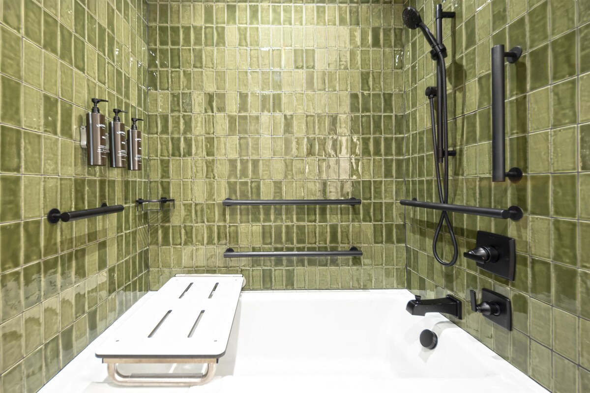 Un bagno con pareti rivestite di piastrelle verdi, una vasca da bagno bianca e accessori neri.