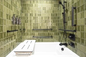 Un bagno con pareti rivestite di piastrelle verdi, una vasca da bagno bianca e accessori neri.