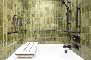 Un baño con paredes de azulejos verdes, una bañera blanca y accesorios negros.