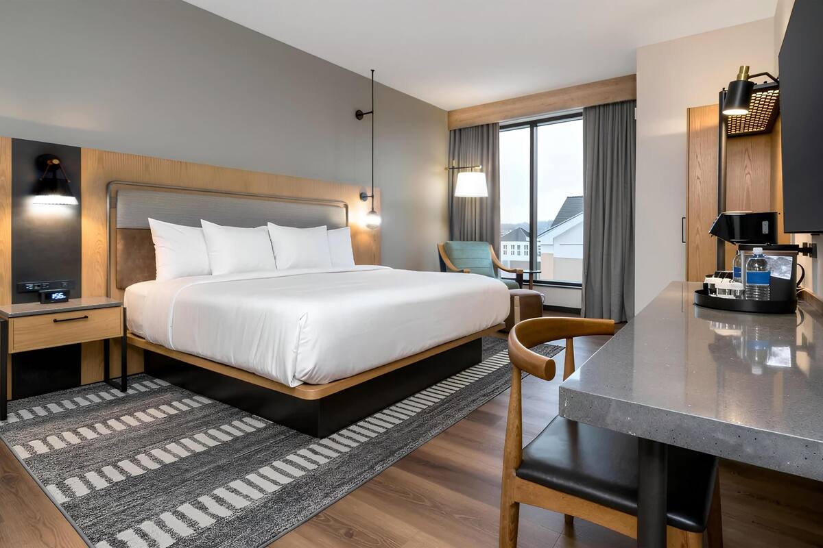 Une chambre d’hôtel comprenant un lit, une table de chevet, une lampe, une chaise, un bureau et un téléviseur.