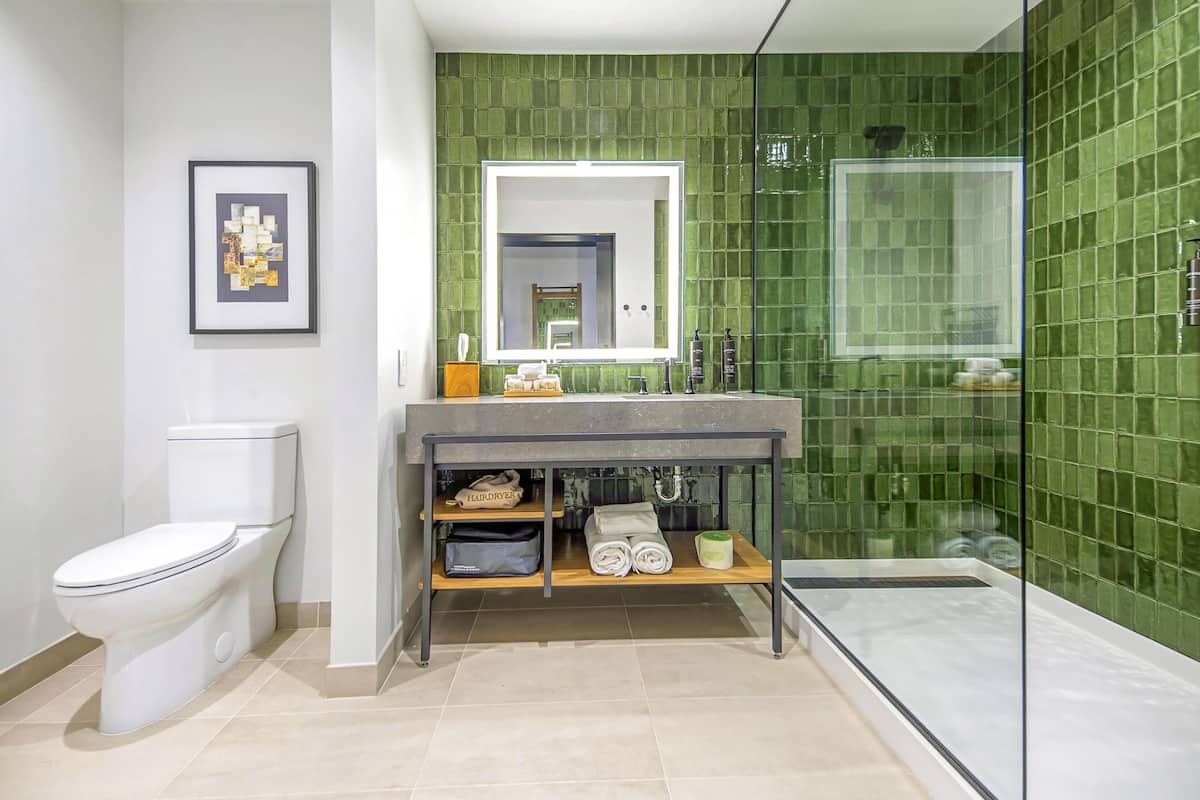 Une salle de bain moderne avec des toilettes, un lavabo avec un miroir, une douche et un mur recouvert de carreaux verts.