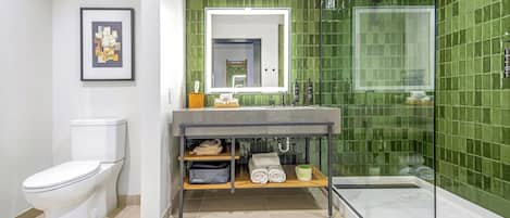 A modern bathroom with a toilet, a sink with a mirror, a shower, and a green tiled wall.