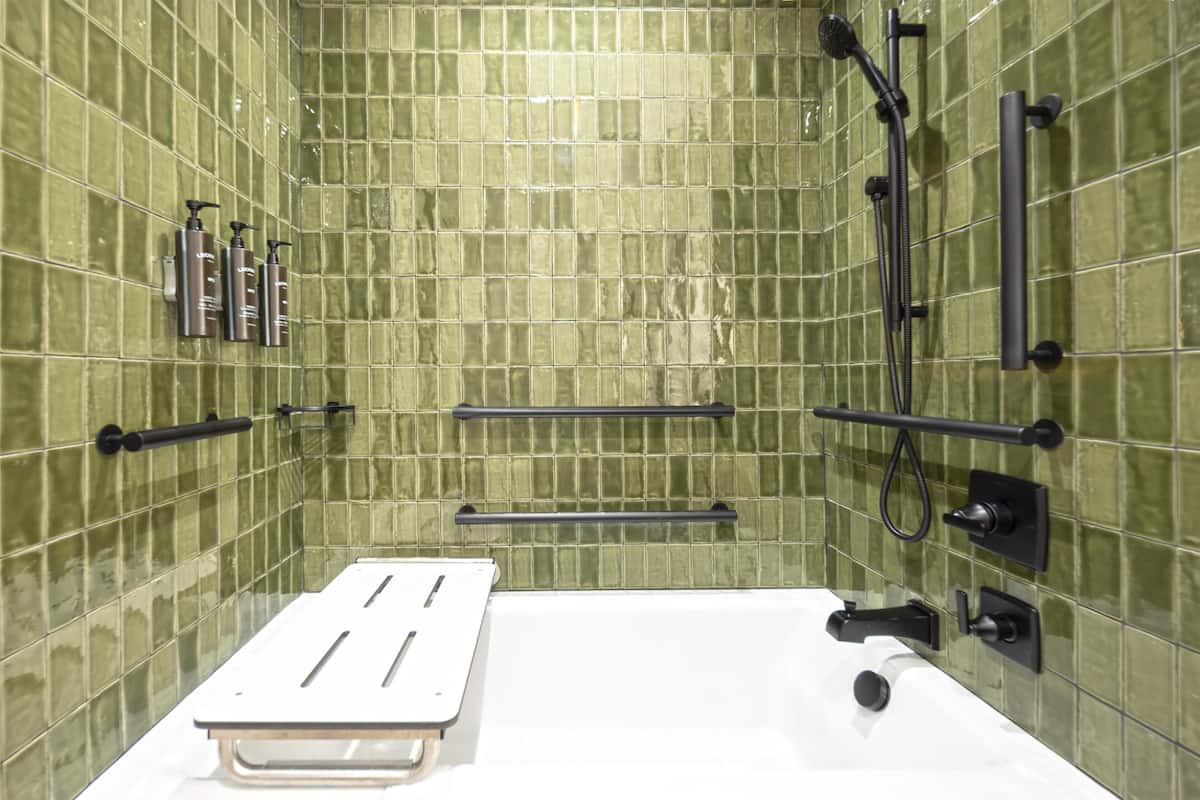 Une salle de bain avec des murs recouverts de carreaux verts, une baignoire blanche et des accessoires noirs.