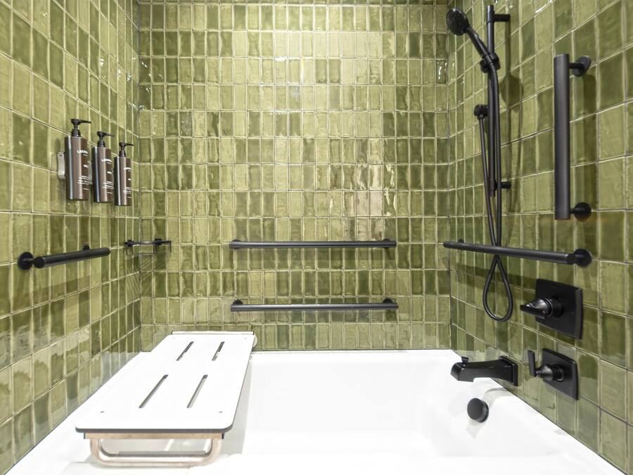 A bathroom with green tiled walls, a white bathtub, and black fixtures.