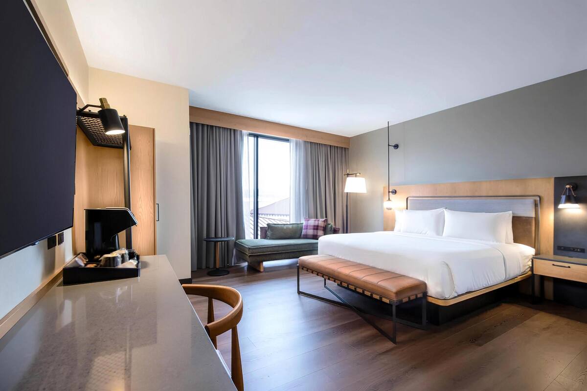 Une chambre d’hôtel équipée d’un lit, d’une table de chevet, d’une lampe, d’une chaise et offrant une vue sur l’extérieur.