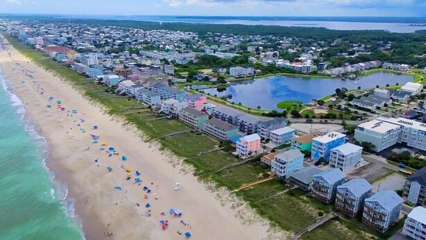 An aerial view of a coastal town with a beach, residential buildings, and a lake.