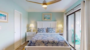 A bedroom with a bed, nightstands, a ceiling fan, and a view through a glass door.