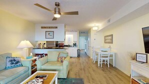 A living room with a sofa, coffee table, and a TV. There is a kitchen area with a dining table and chairs.