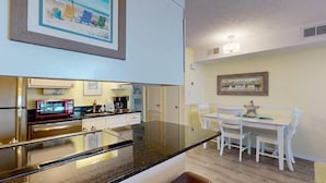 A compact kitchen with a microwave, stove, and white cabinets. There is a dining area with a white table and chairs.