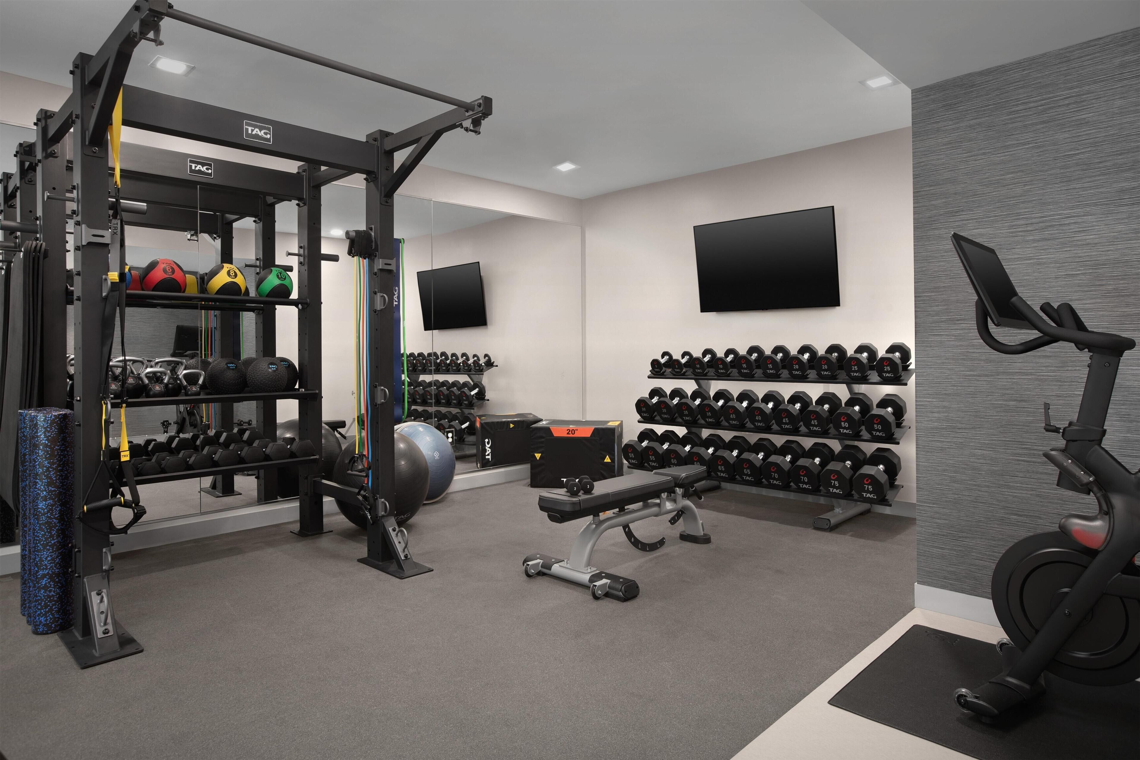 A gym with various exercise equipment, including a squat rack, dumbbells, and a stationary bike.