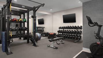 A gym with various exercise equipment, including a squat rack, dumbbells, and a stationary bike.