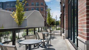 An outdoor patio with round tables and chairs, a brick building in the background, and a clear sky. - Homewood Suites By Hilton Portsmouth Downtown (Portsmouth)