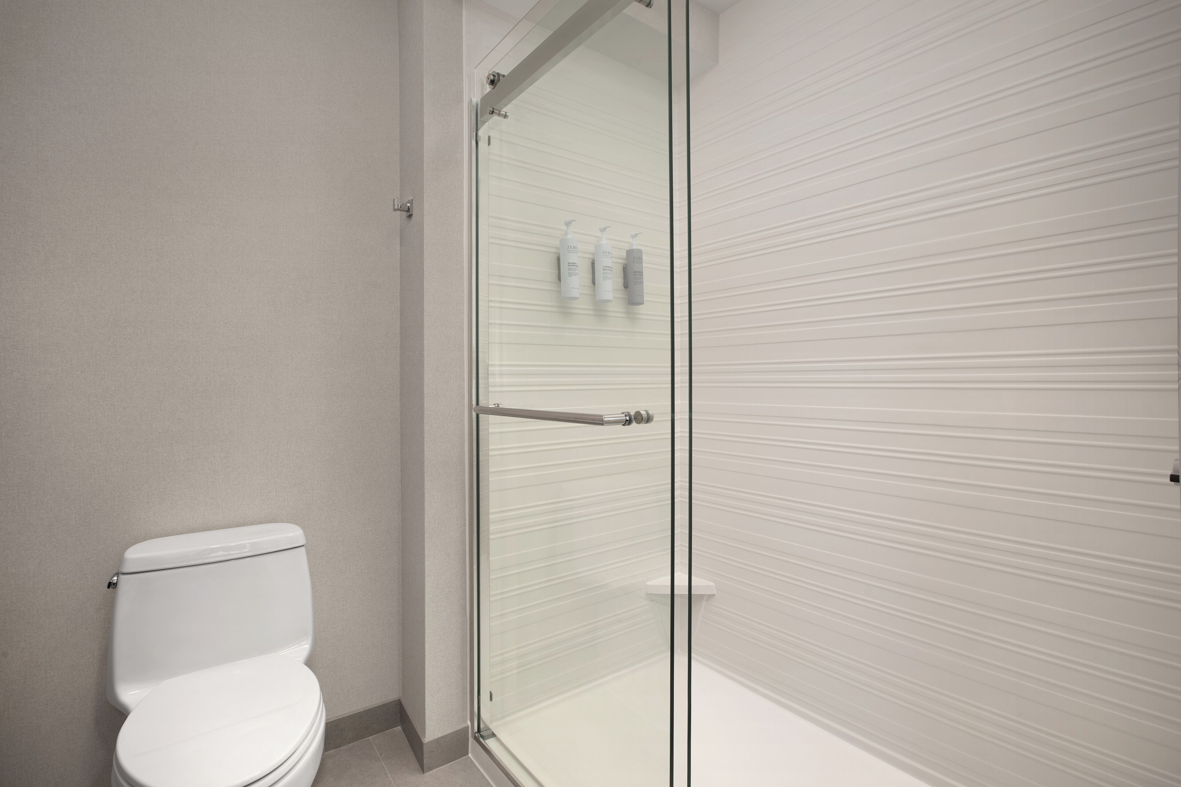 Un baño con inodoro, cabina de ducha de vidrio y un perchero con botellas.