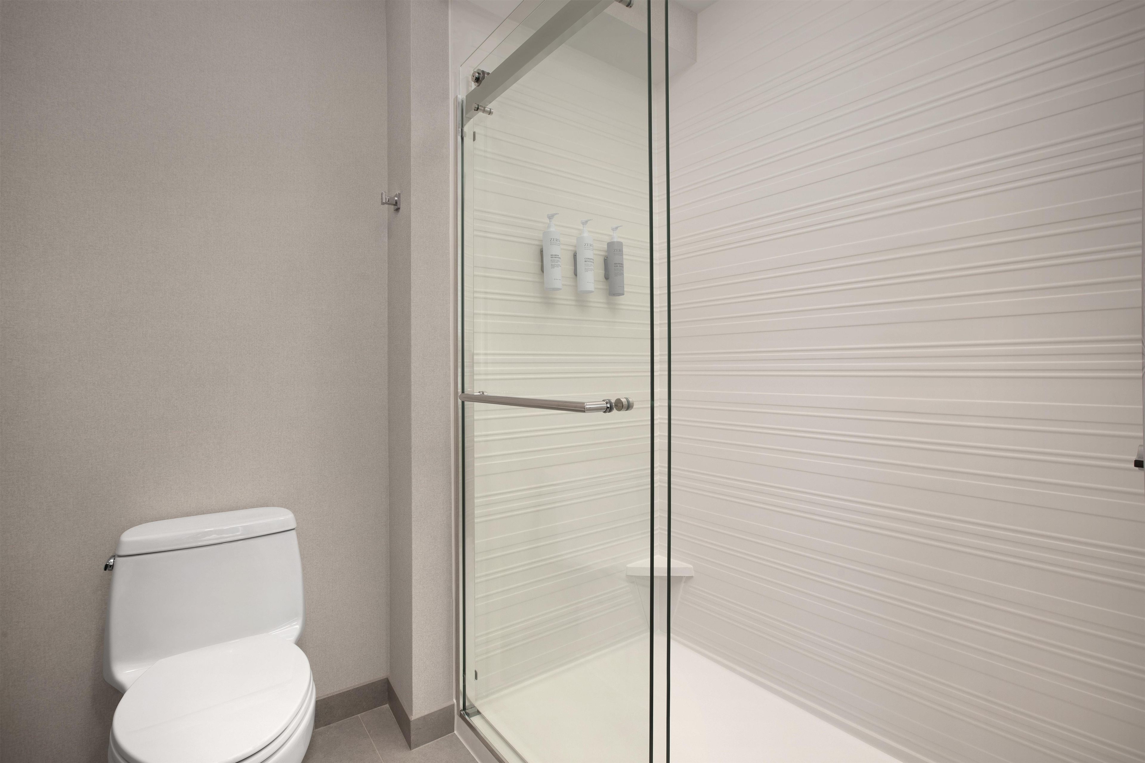 A bathroom with a toilet, a glass shower enclosure, and a towel rack with bottles.