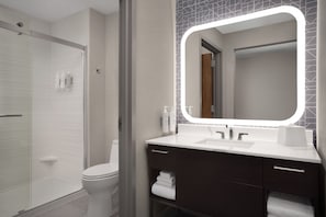 A modern bathroom with a glass shower enclosure, a white toilet, a vanity with dark cabinets, and a large mirror with integrated lighting.