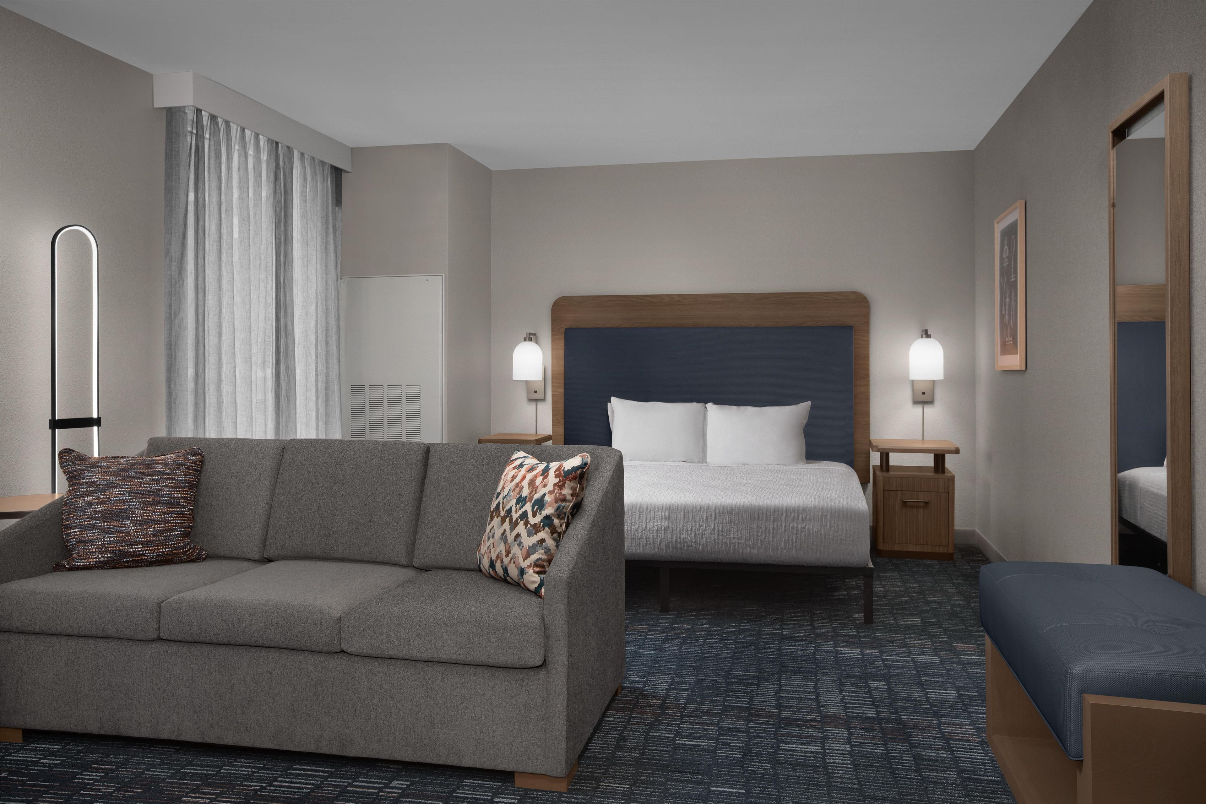 A hotel room with a sofa, a bed, a bedside table, a lamp, and a mirror.