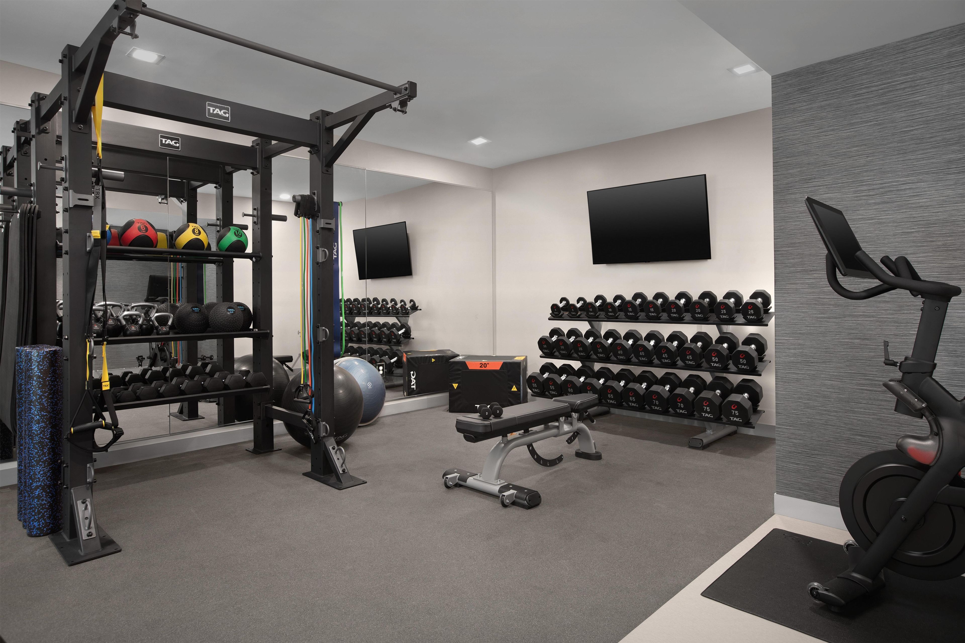 A gym with various exercise equipment, including a squat rack, dumbbells, and a stationary bike.