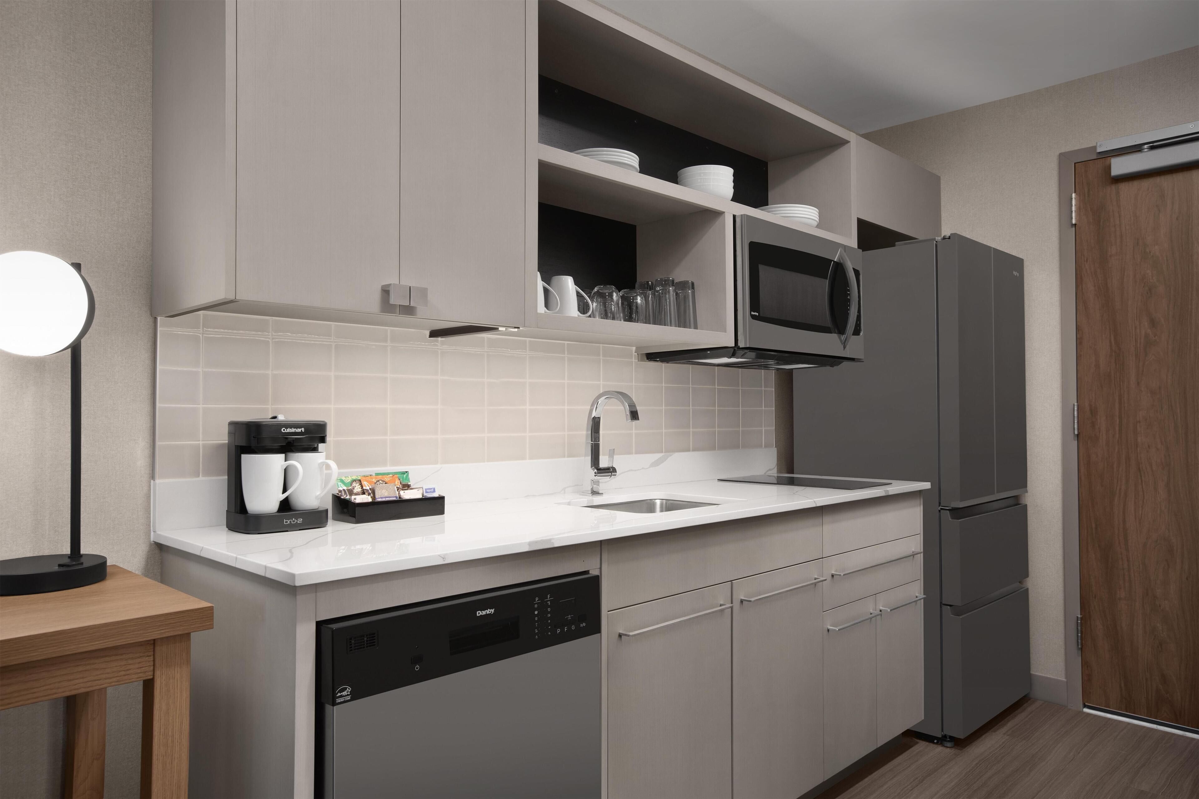 A modern kitchen with grey cabinetry, a built-in microwave, a coffee machine, and a dishwasher.