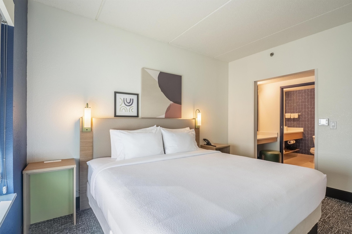 A hotel room with a large bed, bedside tables, a wall-mounted phone, and a bathroom visible through an open door.