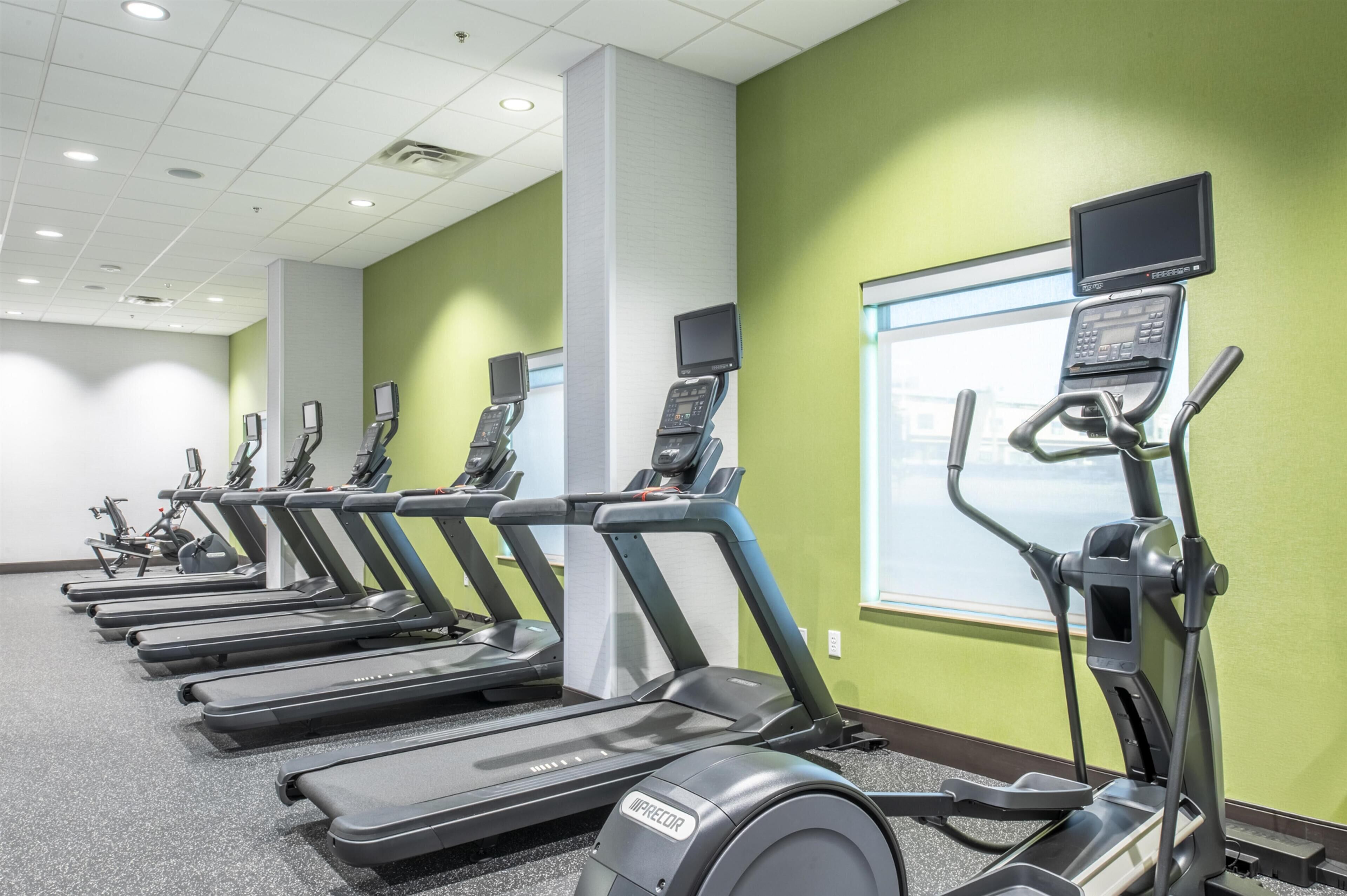 A row of treadmills in a gym with green walls and a window.