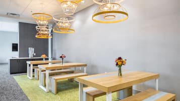 Un espacio de oficina moderno con varias mesas y bancos de madera, alfombra gris y una serie de lámparas colgantes de varios niveles y diseño original.