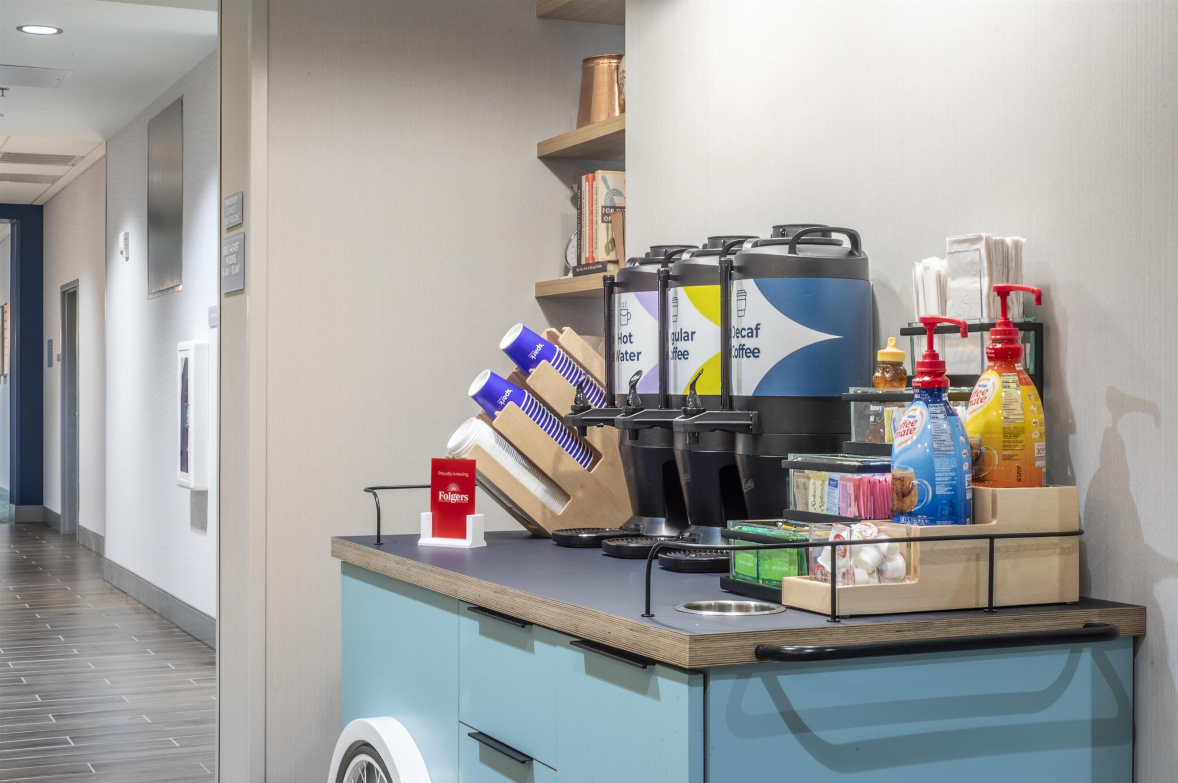 A self-service beverage station with coffee, tea, and water dispensers, a coffee grinder, and condiments.