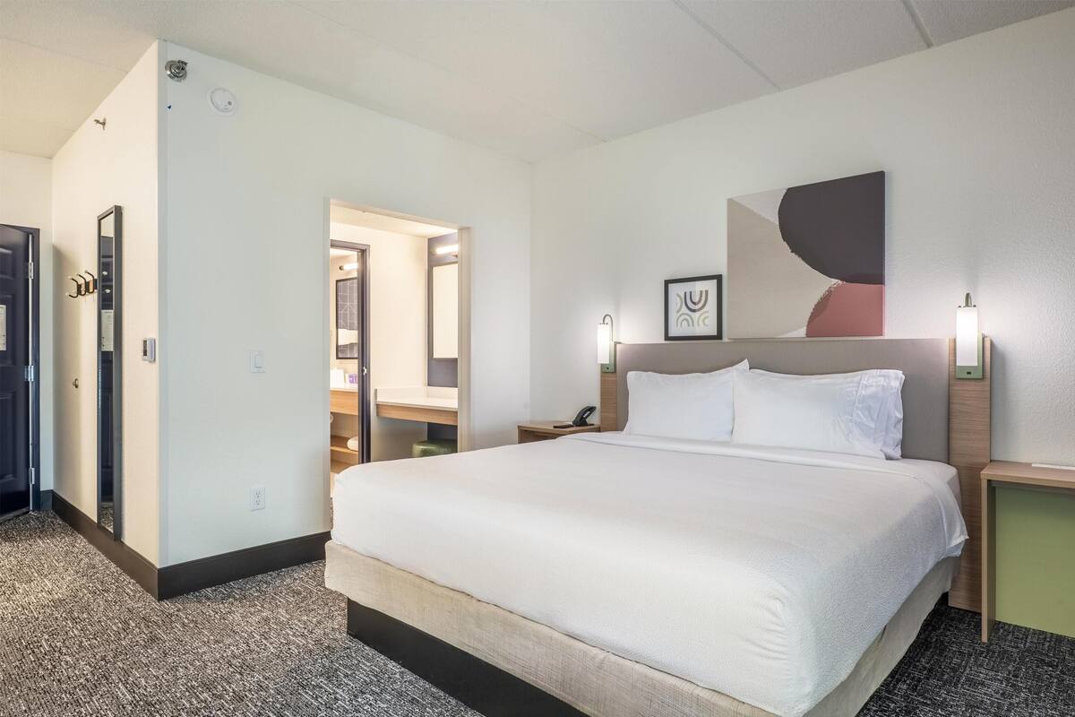 A hotel room with a large bed, bedside tables, a mirror, and a wall-mounted artwork.