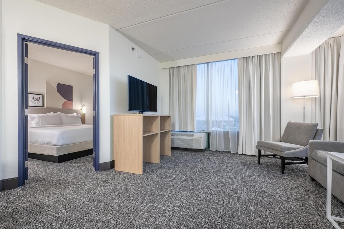 A hotel room with a bed, a TV, a desk, a chair, and a window with curtains.