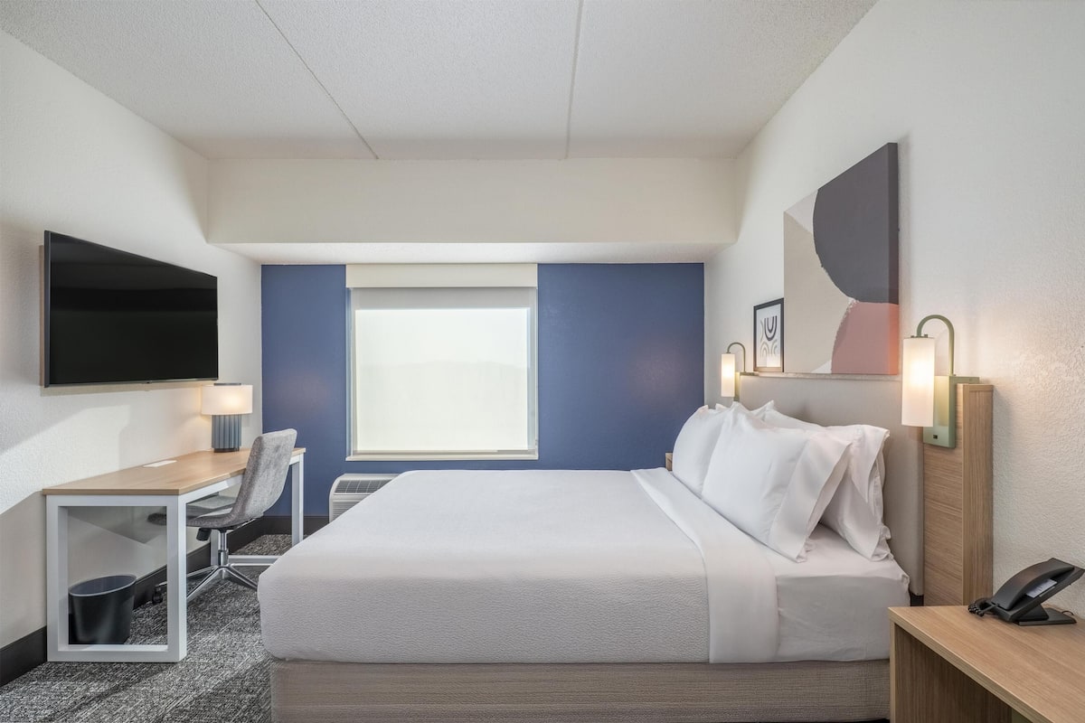 A hotel room with a bed, desk, chair, TV, and a window with curtains.