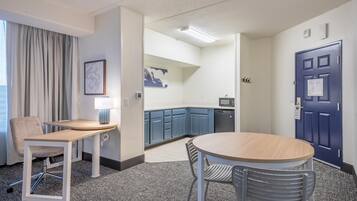 A hotel room with a dining area, kitchenette, and a door with a notice.