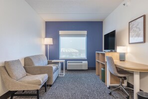 A hotel room with a sofa, a desk, a chair, a TV, and a window with a view. - Spark By Hilton Madison Central (Madison)