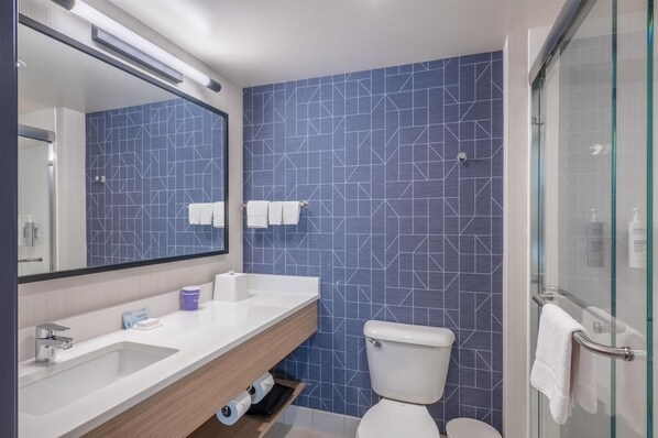 A modern bathroom with a geometric tile backsplash, a white sink, a toilet, and a glass shower enclosure. - Spark By Hilton Madison Central (Madison)