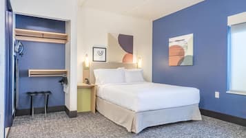 Une chambre à coucher comprenant un lit, des tables de chevet, une commode, un porte-serviettes et des œuvres d’art abstraites accrochées au mur.