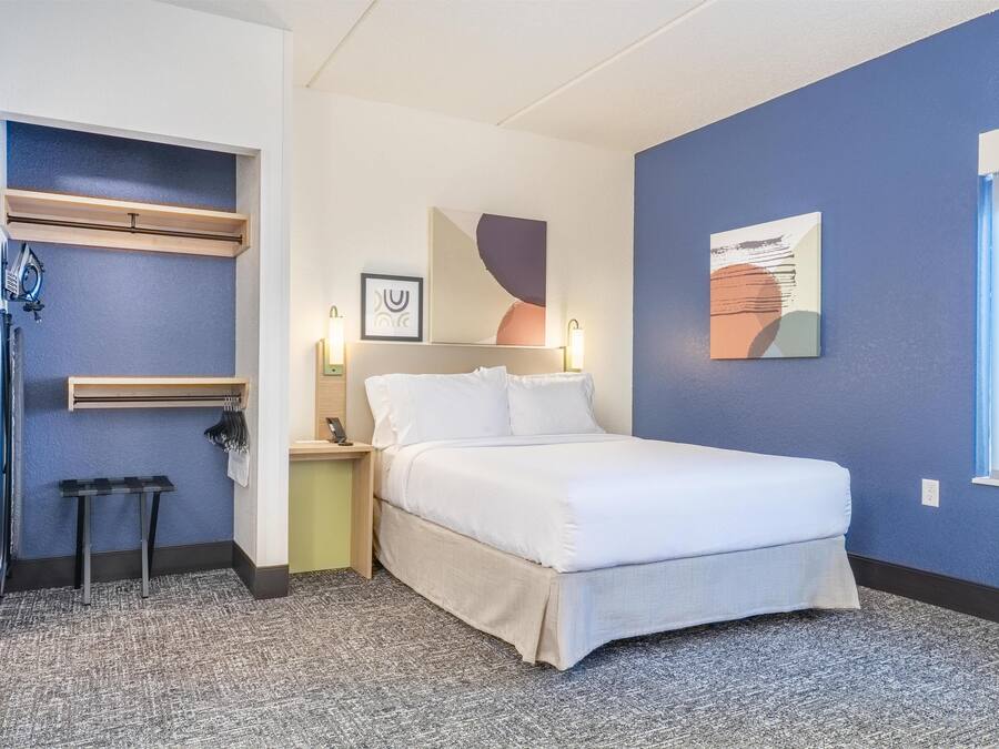 Une chambre à coucher comprenant un lit, des tables de chevet, une commode, un porte-serviettes et des œuvres d’art abstraites accrochées au mur.