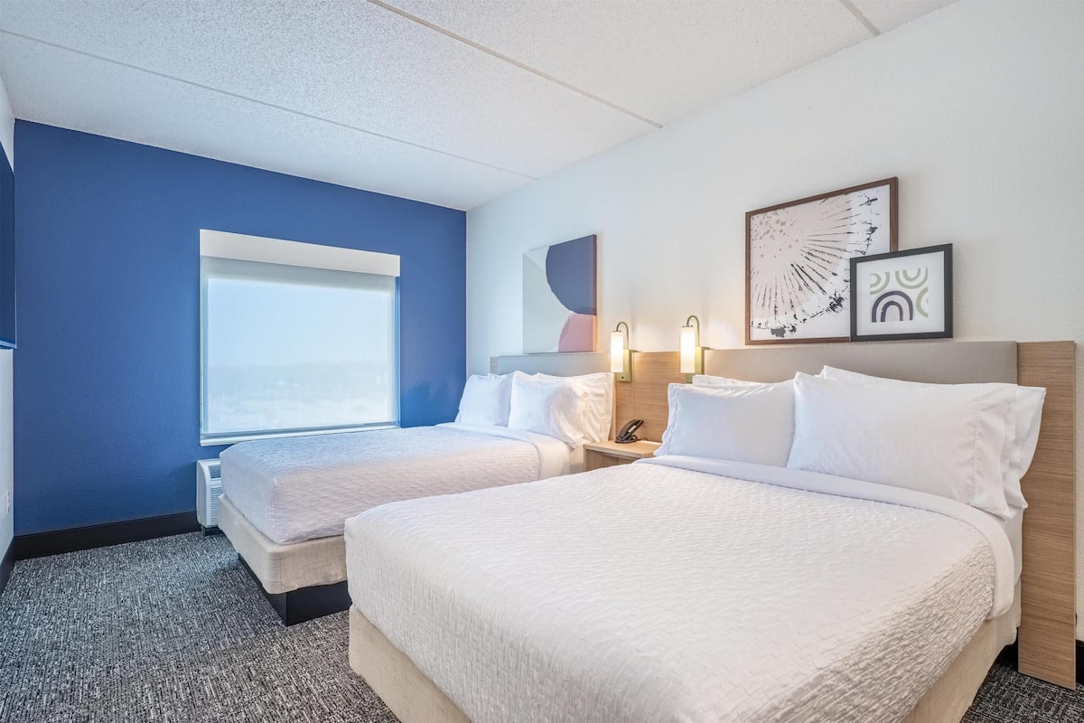 A hotel room with two beds, a large window, and artwork on the wall.